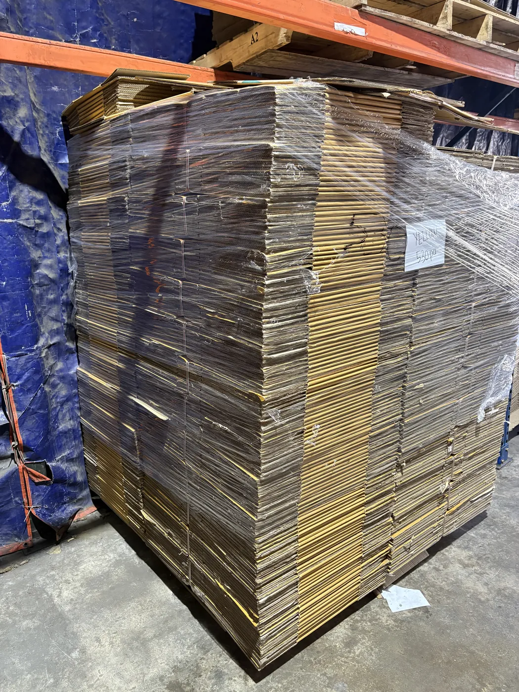 Uma palete cheia de caixas de cartão usadas e dobradas, envolvida em filme e etiquetada "Yellow 520 pcs" no armazém de Balakong.